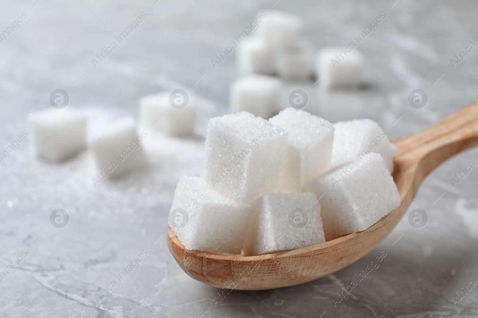 Photo of Refined sugar cubes in spoon on light grey table, closeup