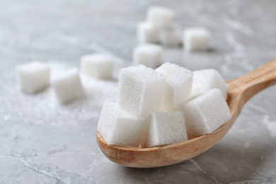 Photo of Refined sugar cubes in spoon on light grey table, closeup