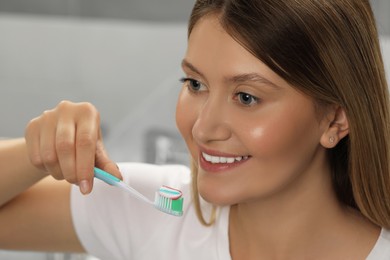Photo of Young woman holding brush with toothpaste in bathroom