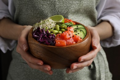 Photo of Woman holding delicious poke bowl with vegetables, fish and edamame beans , closeup