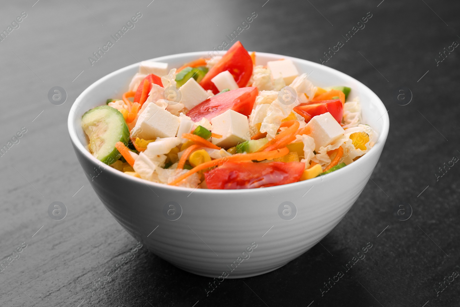 Photo of Tasty salad with Chinese cabbage, carrot, cheese, cucumber, corn and tomato on black table, closeup