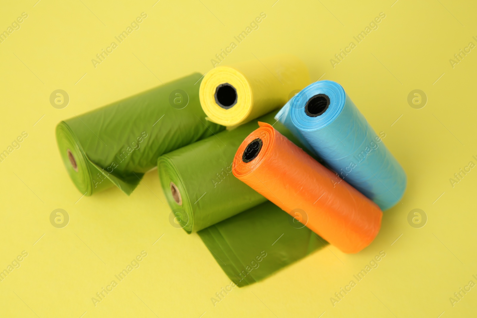 Photo of Colorful dog waste bags on yellow background, above view