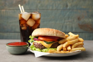 Delicious burger, soda drink and french fries served on grey table