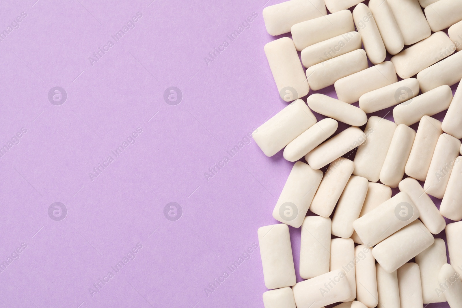 Photo of Many chewing gum pieces on violet background, flat lay. Space for text