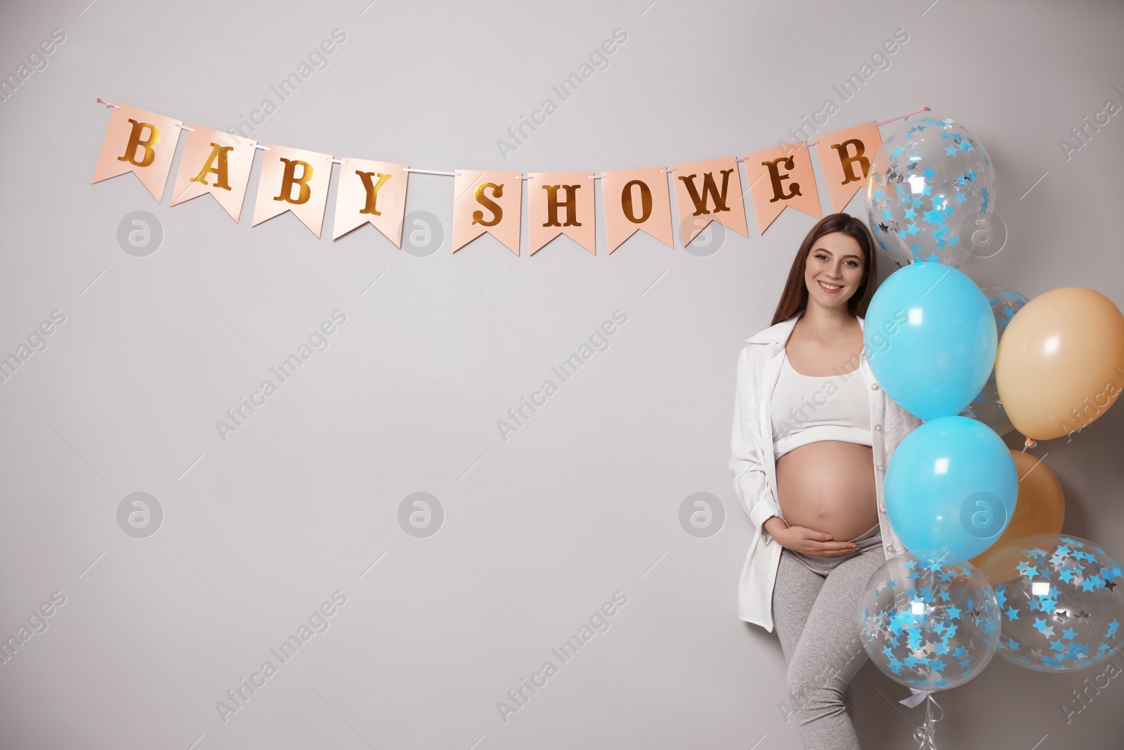 Photo of Happy pregnant woman holding balloons near grey wall with Baby Shower flags, space for text