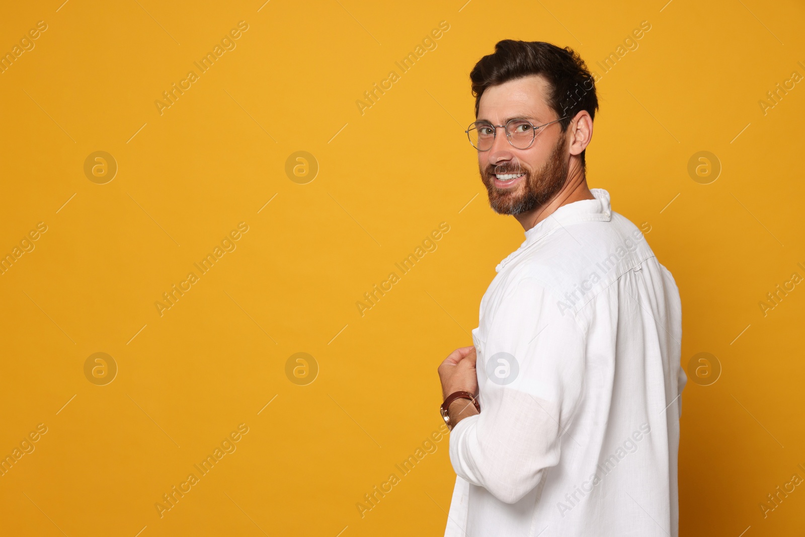 Photo of Portrait of smiling bearded man with glasses on orange background. Space for text