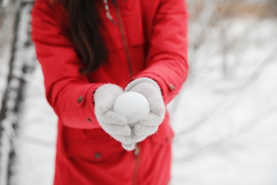 Photo of Young woman holding snowball outdoors on winter day, closeup