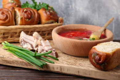 Photo of Delicious borsch served with pampushky and salo on wooden table, closeup. Traditional Ukrainian cuisine
