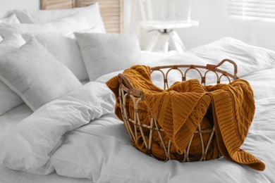 Basket with warm knitted plaid on bed indoors