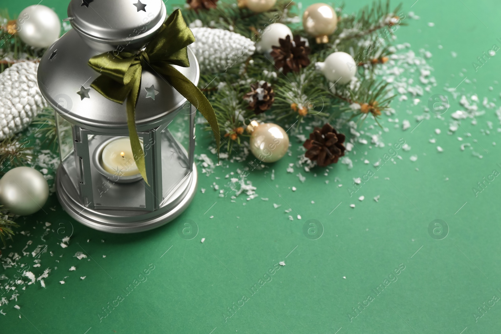 Photo of Christmas lantern with burning candle and festive decor on green background