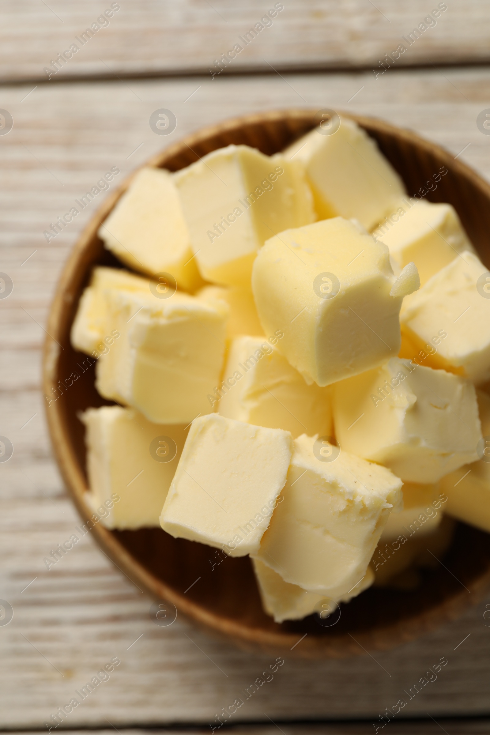 Photo of Tasty butter cubes in bowl on light wooden table, top view