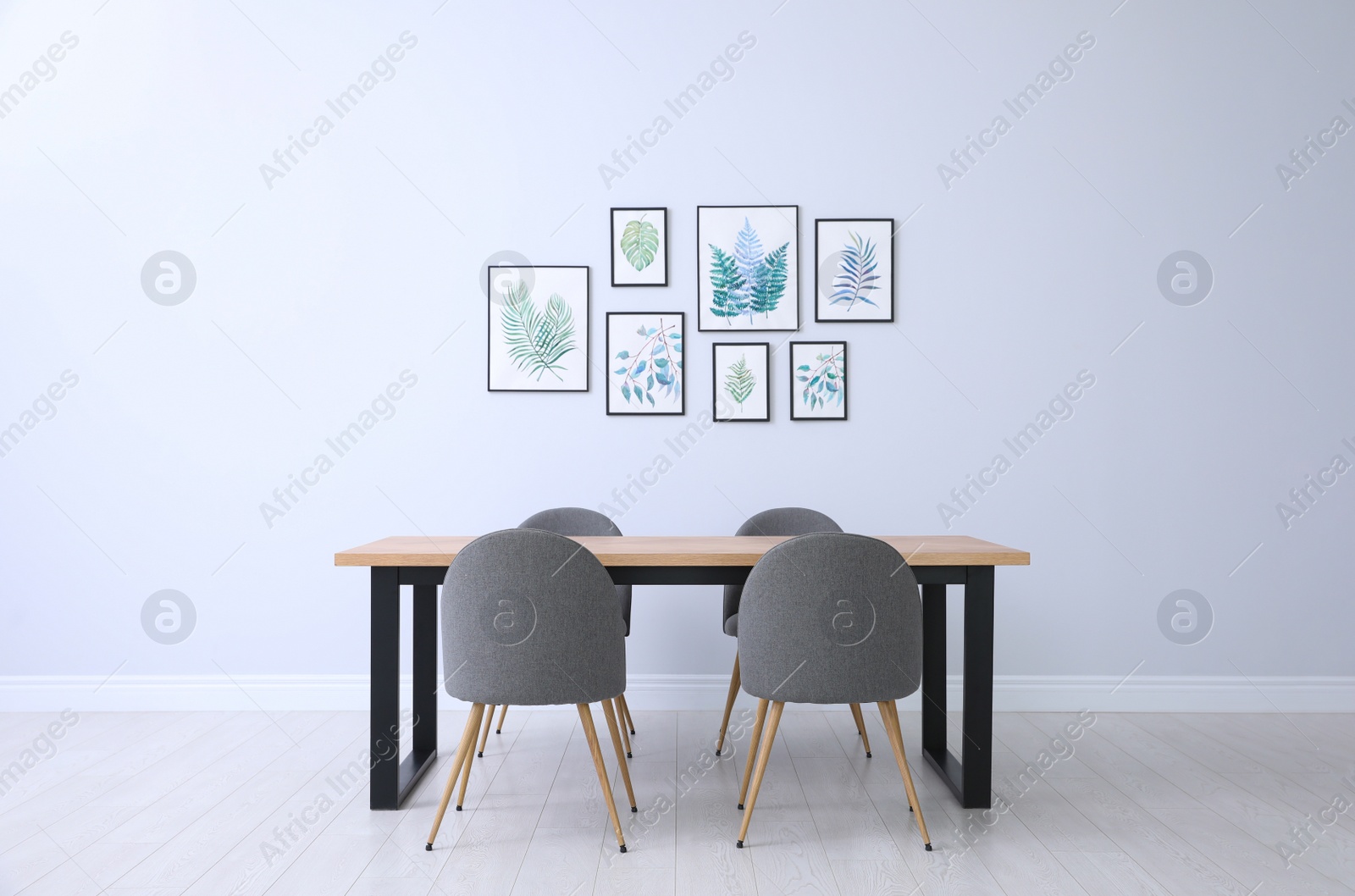 Photo of Stylish room interior with modern table, chairs and paintings of tropical leaves. Idea for design