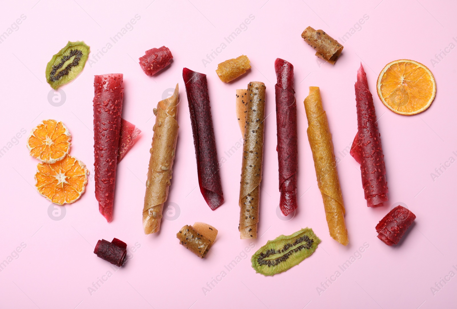 Photo of Delicious fruit leather rolls on pink background, flat lay