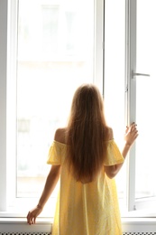 Young beautiful woman opening big window in room