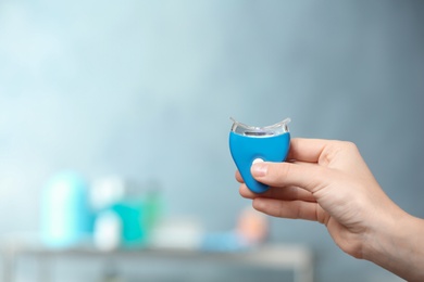 Photo of Woman holding teeth whitening device on blurred background. Space for text