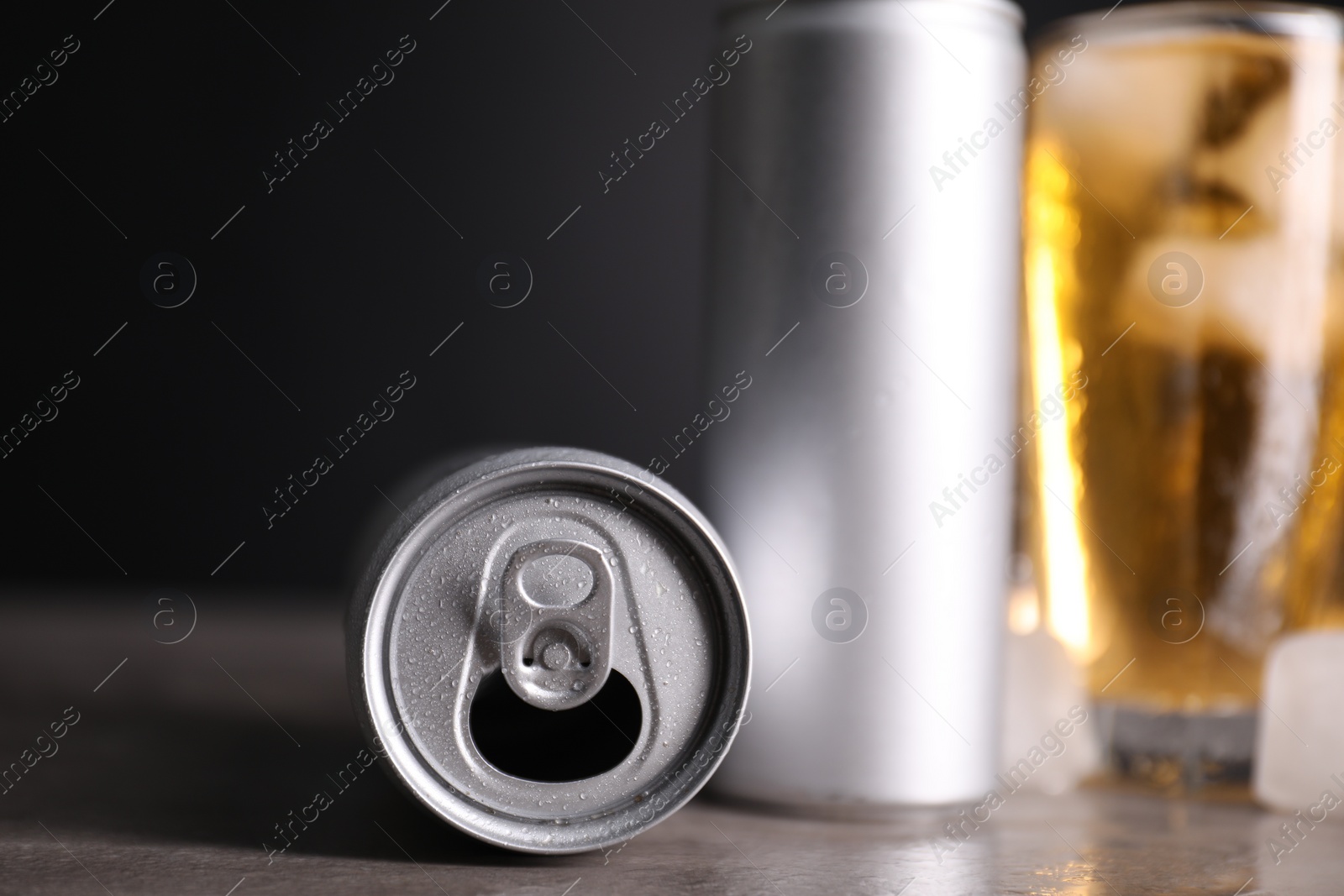 Photo of Tasty energy drink with ice cubes in glass and aluminium cans on grey table, closeup