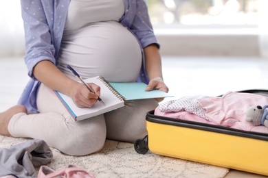 Photo of Pregnant woman writing packing list for maternity hospital at home, closeup