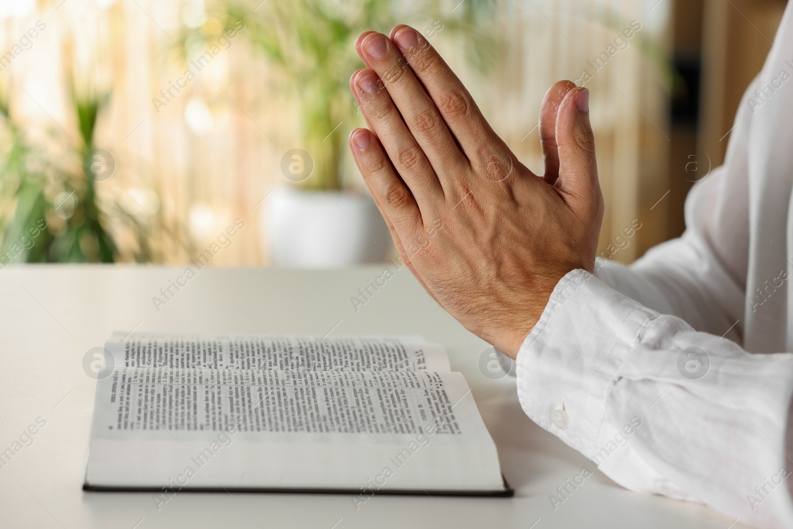 Photo of Man with Bible praying at white table indoors, closeup