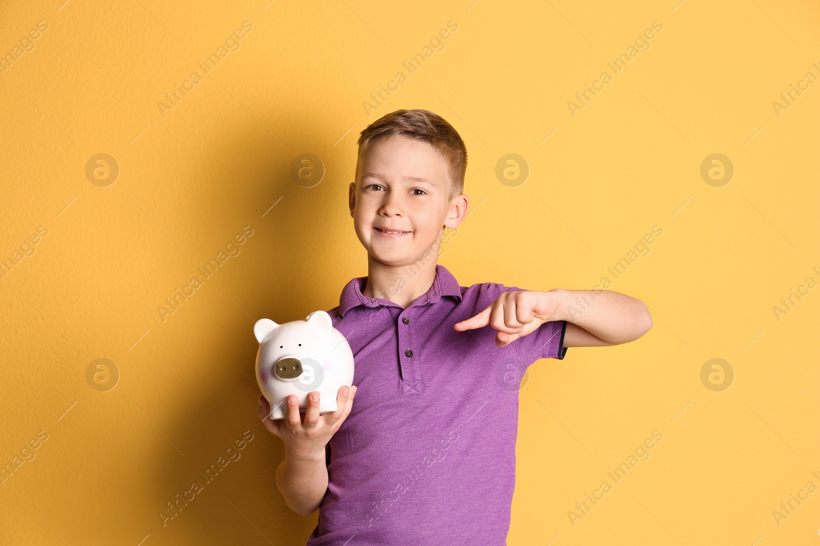 Photo of Little boy with piggy bank on color background