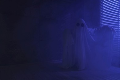 Photo of Creepy ghost. Woman covered with sheet near window in blue light, space for text