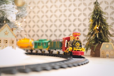 Photo of Toy train and railway near Christmas tree indoors