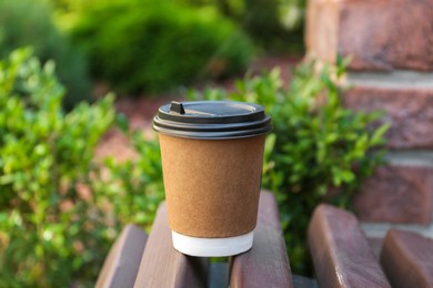 Photo of Disposable paper cup with plastic lid on wooden bench outdoors