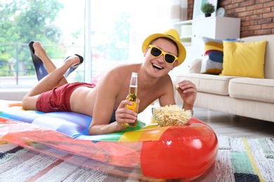 Photo of Shirtless man with inflatable mattress, drink and popcorn on floor at home