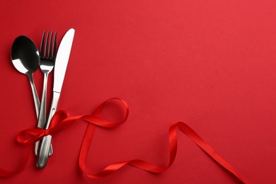 Cutlery set and ribbon on red background, flat lay with space for text. Valentine's Day dinner