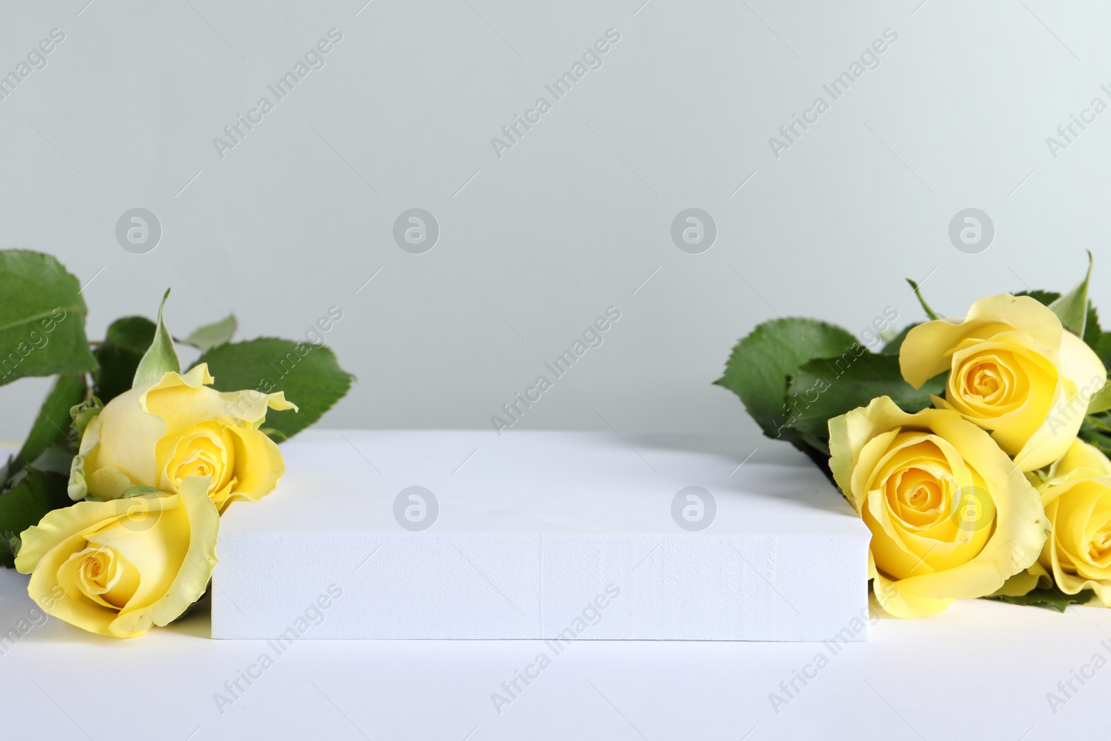 Photo of Beautiful presentation for product. Square podium and yellow roses on white table against light grey background, space for text