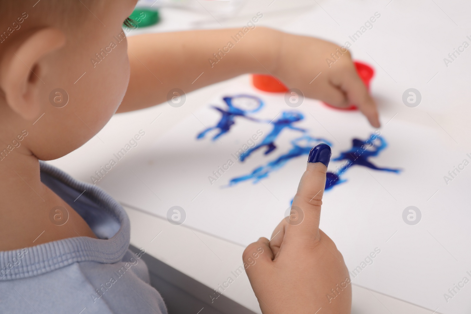 Photo of Little boy painting with finger at white table indoors, closeup