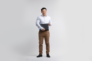 Full length portrait of happy man with laptop on light background