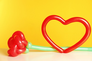 Rose and heart figures made of modelling balloons on table against color background