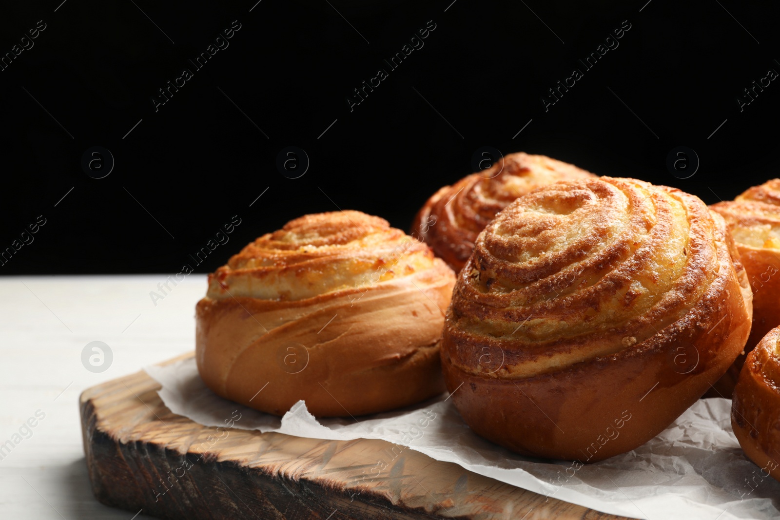 Photo of Wooden board with tasty buns on table against black background. Fresh from oven