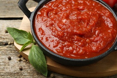 Photo of Homemade tomato sauce in bowl and basil on wooden table, closeup