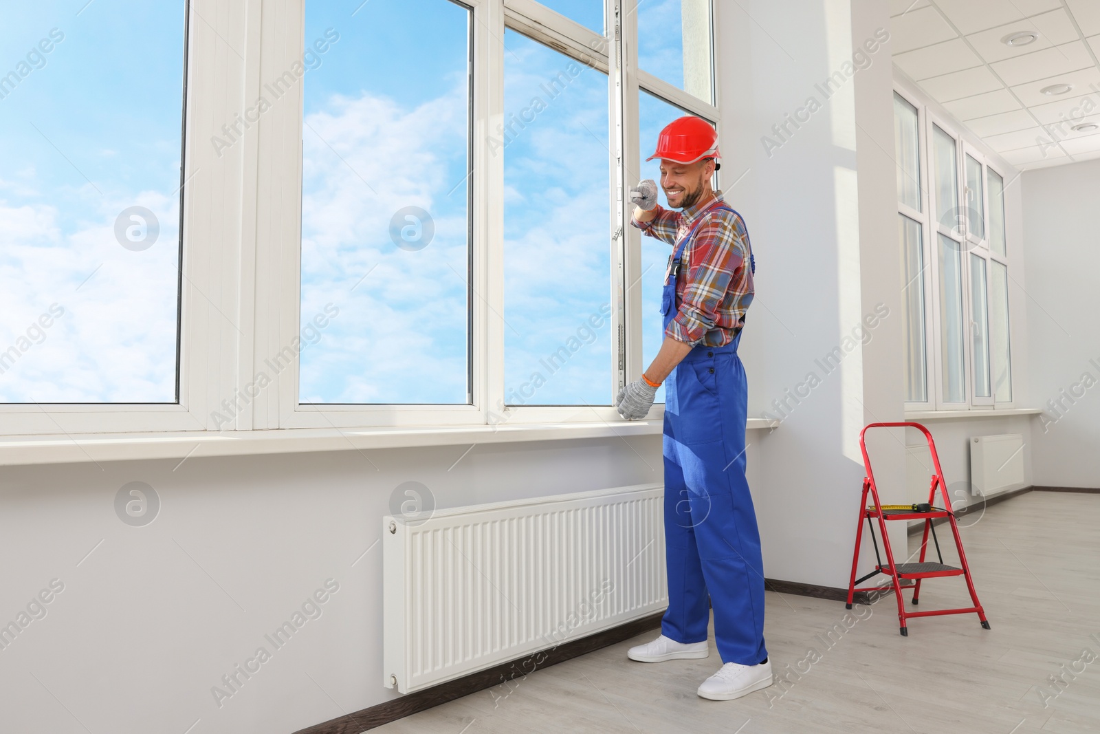 Photo of Worker in uniform installing plastic window indoors