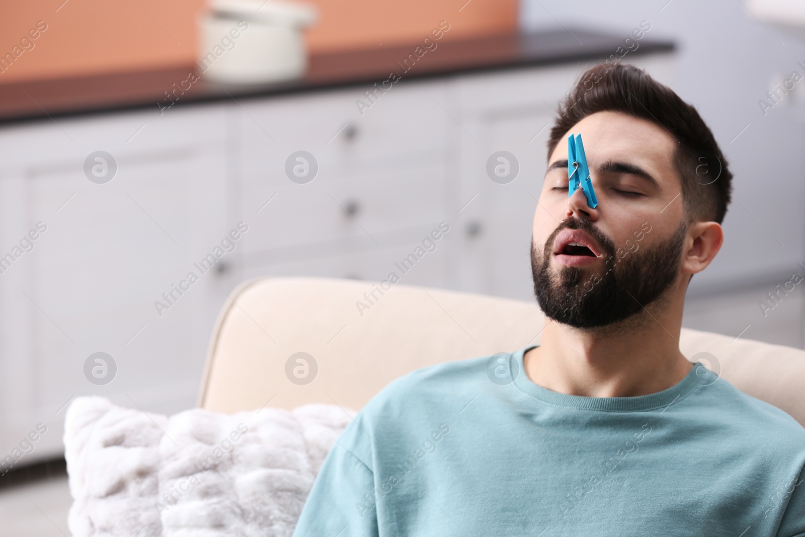 Photo of Man with clothespin suffering from runny nose at home. Space for text