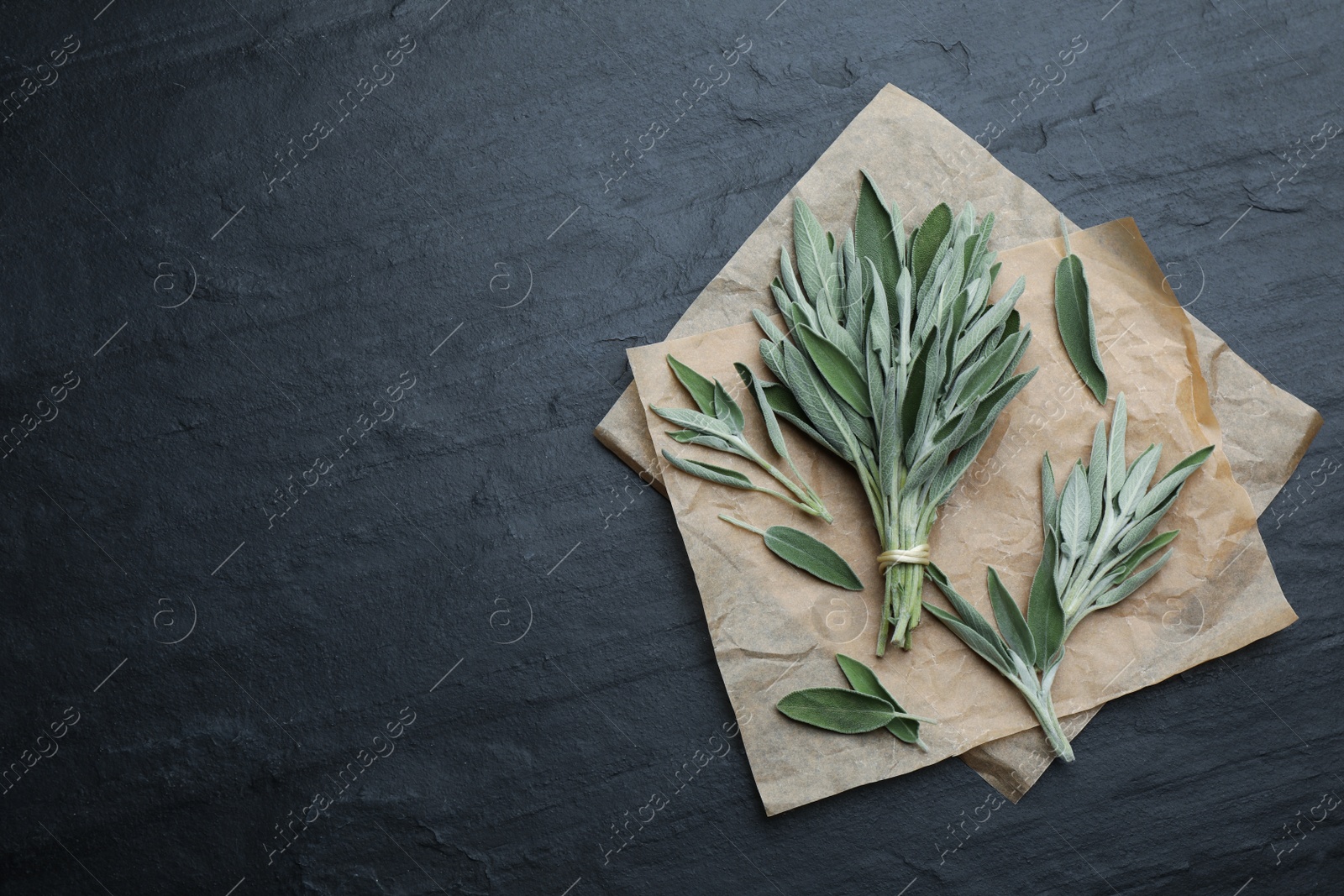 Photo of Fresh green sage with parchment on black table, flat lay. Space for text
