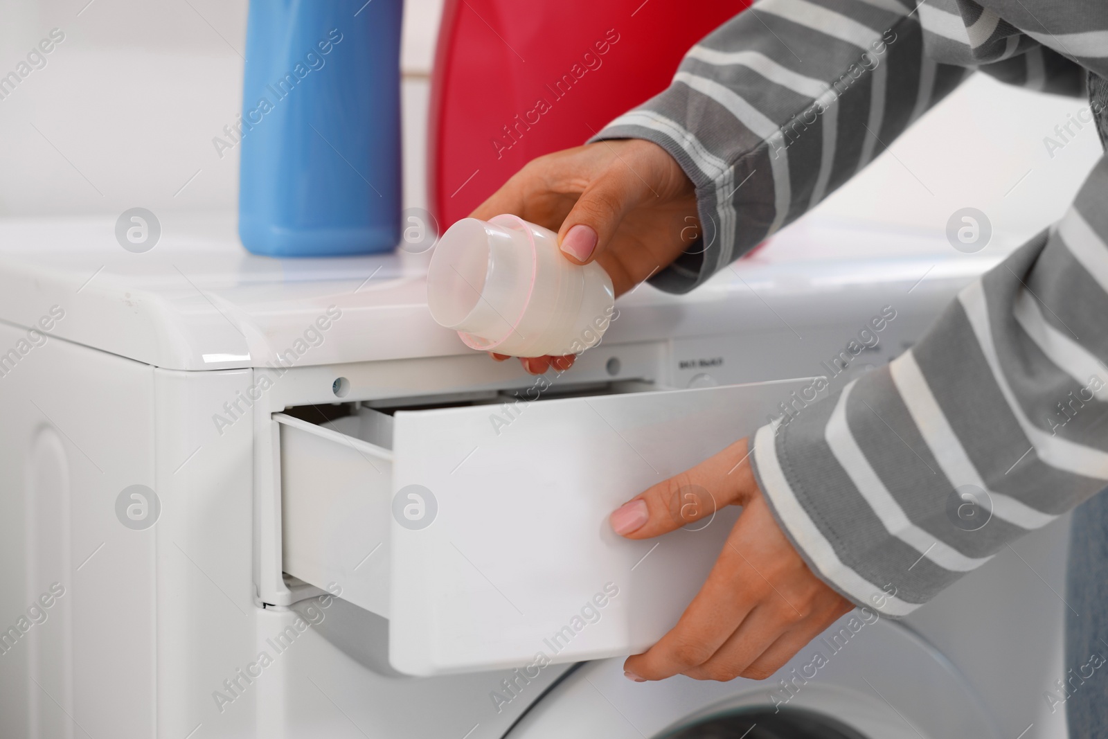 Photo of Woman pouring laundry detergent into washing machine indoors, closeup