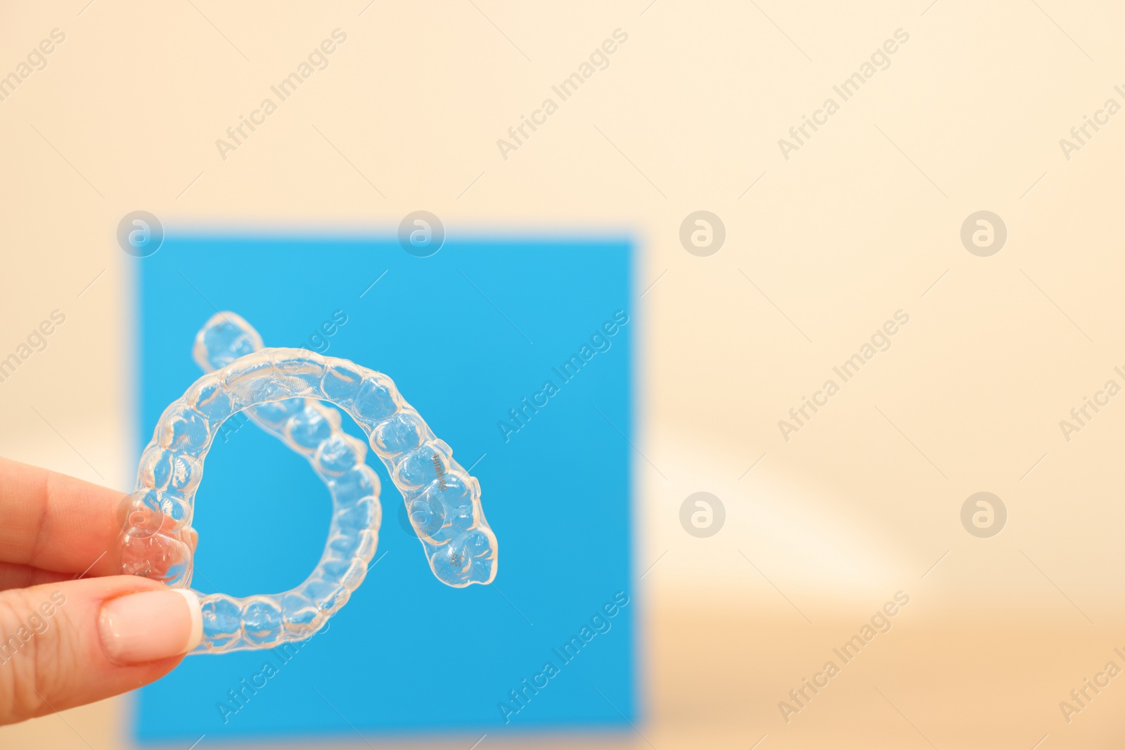 Photo of Woman with transparent dental aligners on blurred background, closeup. Space for text