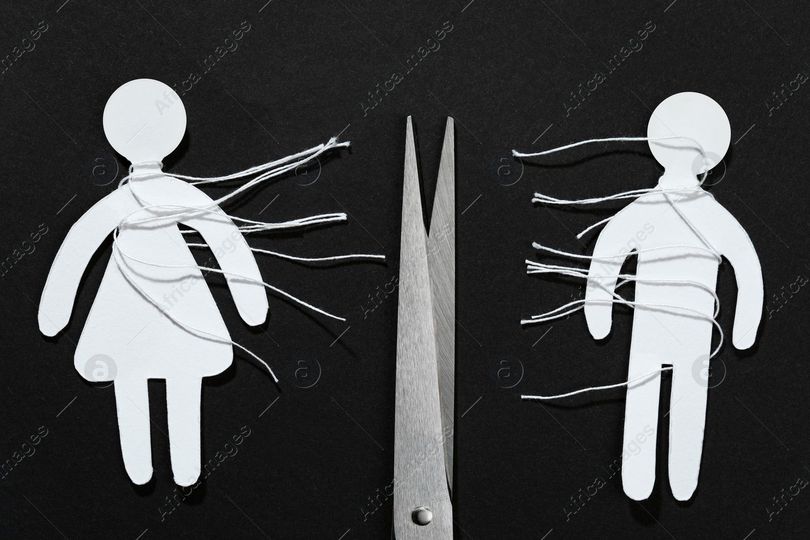 Photo of Divorce concept. Paper human figures with cut white threads and scissors on black background, flat lay
