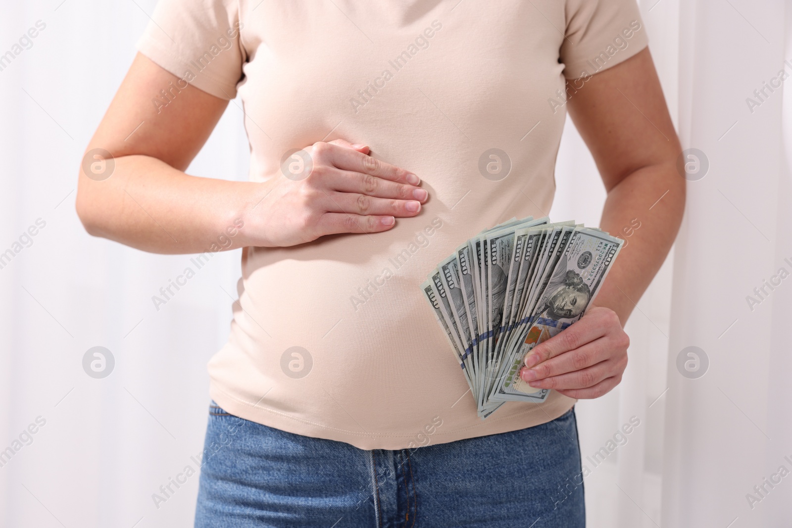 Photo of Surrogate mother. Pregnant woman with dollar banknotes indoors, closeup