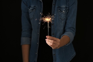 Photo of Woman holding burning sparklers on black background, closeup