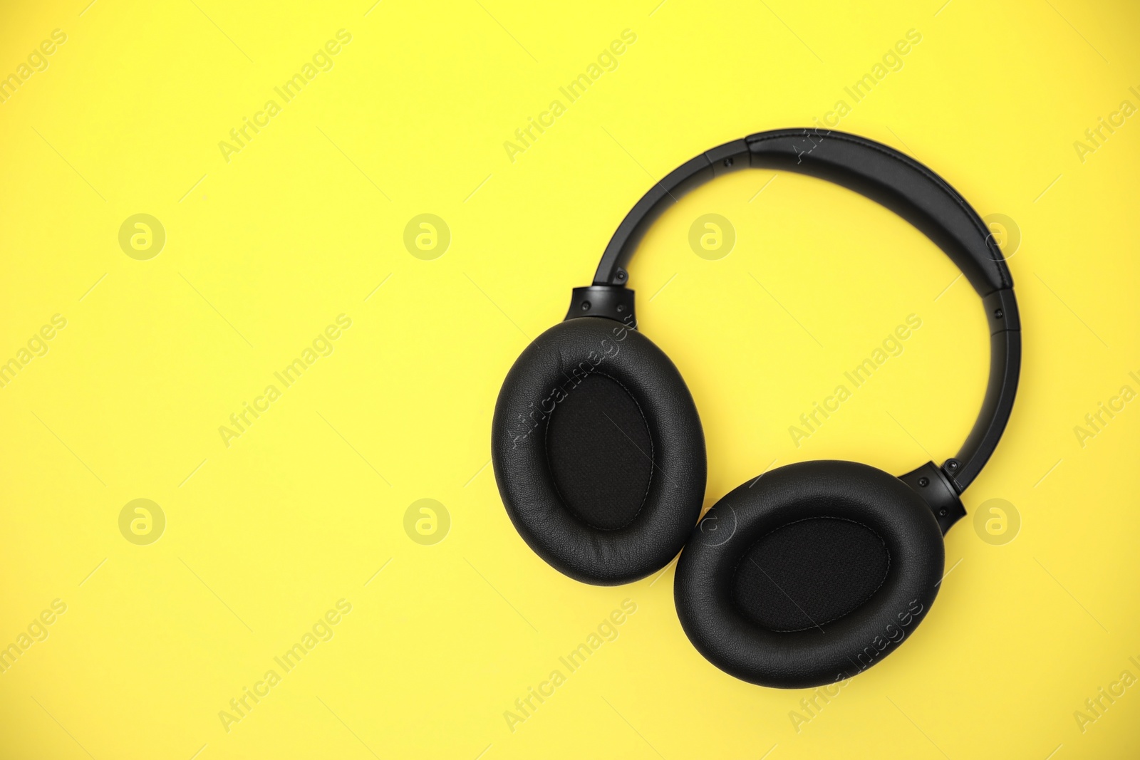 Photo of Modern wireless headphones on yellow background, top view. Space for text