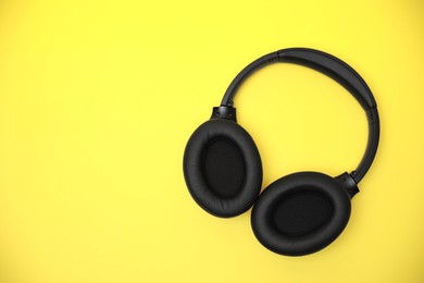 Photo of Modern wireless headphones on yellow background, top view. Space for text