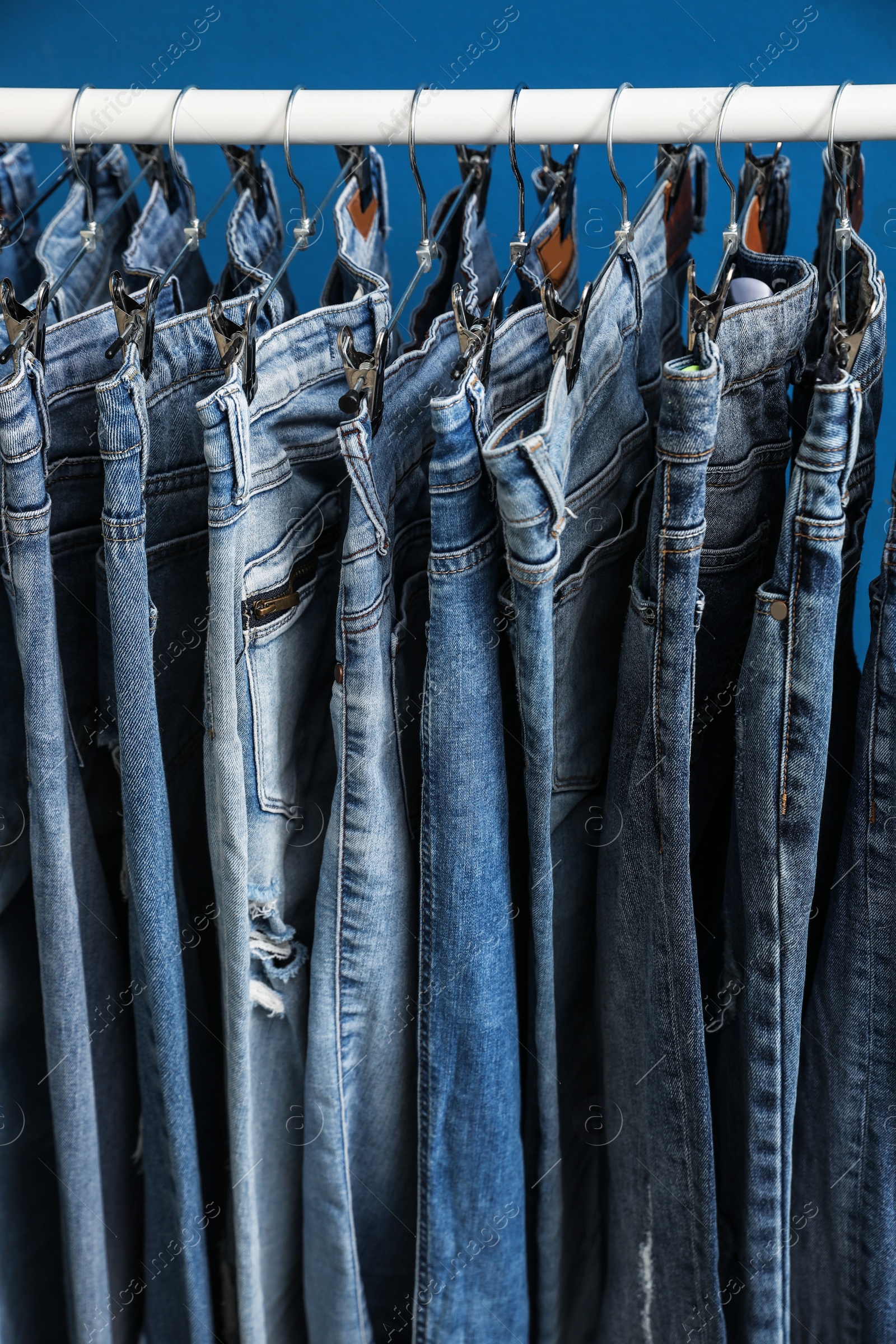 Photo of Rack with stylish jeans on blue background, closeup