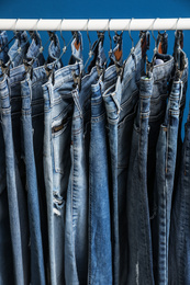 Rack with stylish jeans on blue background, closeup