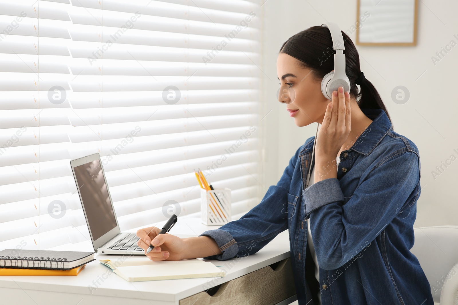 Photo of Online translation course. Student in headphones writing near laptop at home