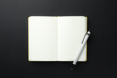 Photo of Open notebook with blank pages and pen on black background, top view. Space for text