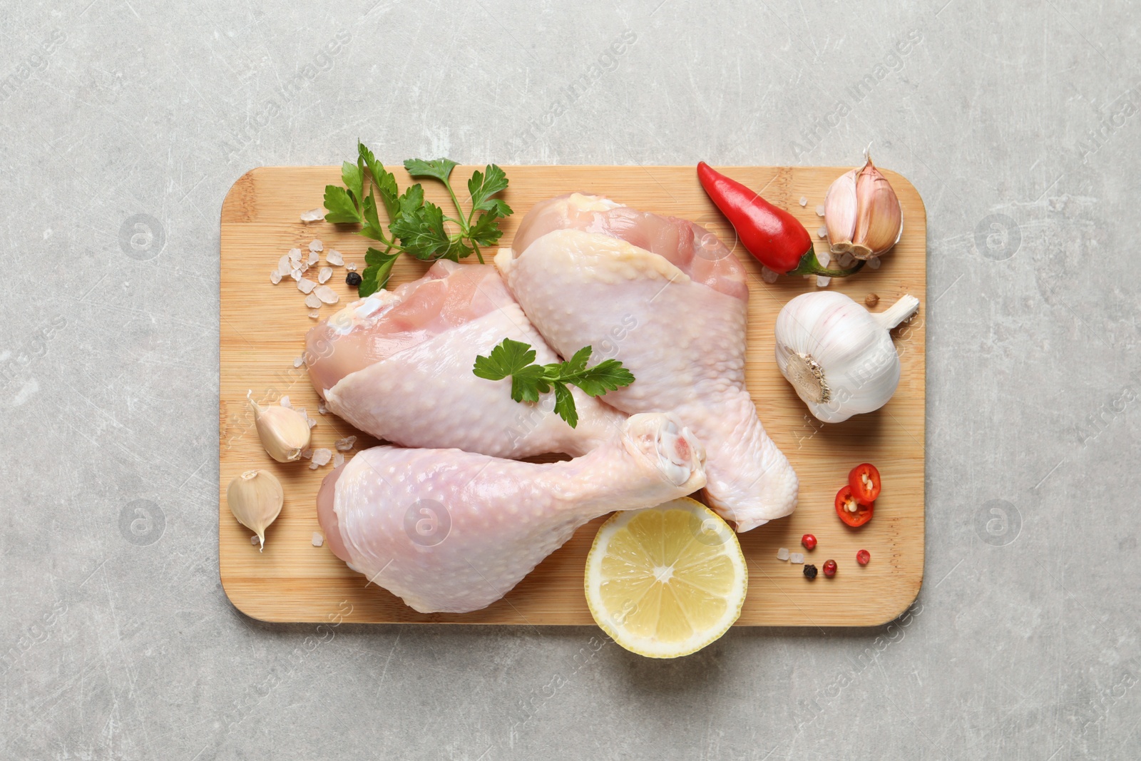 Photo of Wooden board with fresh raw chicken legs and other products on light grey table, top view