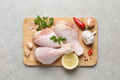 Photo of Wooden board with fresh raw chicken legs and other products on light grey table, top view